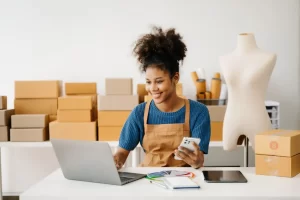 A young business owner checking is using her phone and laptop to check for the best equipment finance options online