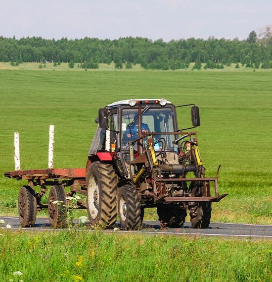 A tractor towing a hay bail trailer is driving up the road between farming paddocks