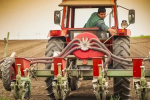 A view from rear aspect of a farmer driving his tractor looking around at the planting attachment on his tractor that he's considering upgrading